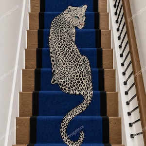 Könnte beinhalten: Ein blauer Treppenläufer mit schwarzem Rand und Leopardenmuster. Der Leopard sitzt mit einem gefleckten Muster und grünen Augen. Die Treppe ist aus Holz.