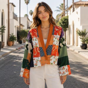 Peut inclure: Une veste en patchwork composée de divers carrés de tissu dans des tons orange, vert, blanc et bleu foncé. Le vêtement présente un col châle orange uni, des manches longues et une coupe ouverte sans boutons portée sur un haut blanc uni.