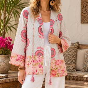 May include: A light blue open-front jacket featuring a repeating pink and dark red floral pattern on the upper section and a dense pink floral print on the lower hem. The jacket includes long sleeves, a shawl collar, and two thin hanging tassels.
