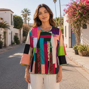 May include: A long-sleeved jacket featuring a vibrant patchwork design with rectangular panels in shades of pink, green, purple, orange, black, and white. The garment includes a round neckline, a front closure with two toggle buttons, and green trim.