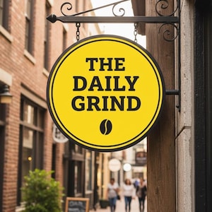 Peut inclure: Un panneau circulaire jaune avec les mots "THE DAILY GRIND" en noir et un motif de grain de caf&eacute;. Le panneau est suspendu &agrave; un support en m&eacute;tal noir avec des volutes d&eacute;coratives. L'arri&egrave;re-plan montre un b&acirc;timent en briques et une all&eacute;e pi&eacute;tonne.