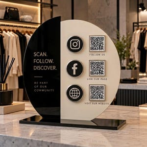 May include: A circular black and cream acrylic sign on a rectangular base. The black side features the text SCAN. FOLLOW. DISCOVER. BE PART OF OUR COMMUNITY. The cream side displays three social media icons and three QR codes with labels.