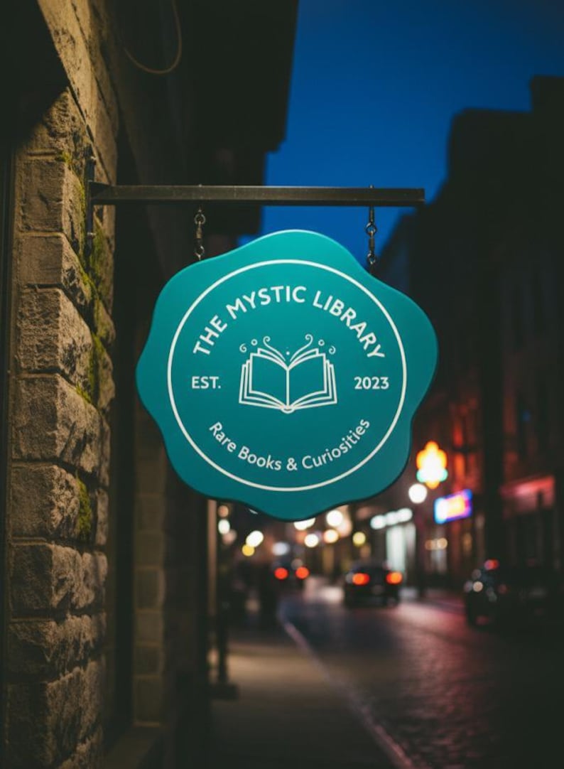 Peut inclure: Un panneau turquoise pour "The Mystic Library" est suspendu &agrave; un b&acirc;timent en briques. Le panneau a une forme unique avec du texte blanc et un dessin de livre ouvert. Le panneau indique "Rare Books & Curiosities" et "Est. 2023".