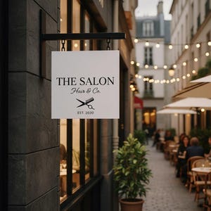 Peut inclure: Un panneau carr&eacute; blanc pour "The Salon Hair & Co." est suspendu &agrave; un support noir. Le panneau affiche le nom du salon, un graphisme de ciseaux et de peigne, et l'ann&eacute;e d'&eacute;tablissement, 2020. Le panneau est fix&eacute; &agrave; un b&acirc;timent gris fonc&eacute;.