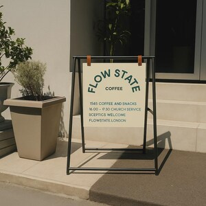 May include: An outdoor sign for "Flow State Coffee" with a black metal frame and a cream-colored sign. The sign has the business name, "Coffee", and service details in a dark green font. The sign is held by brown leather straps.
