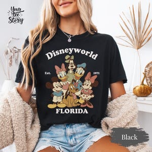May include: Black t-shirt featuring a vintage-style Disney World graphic with Mickey Mouse, Minnie Mouse, Donald Duck, Daisy Duck, Goofy, and Pluto. The text "Disneyworld Florida Est. 1971" is printed above the characters.