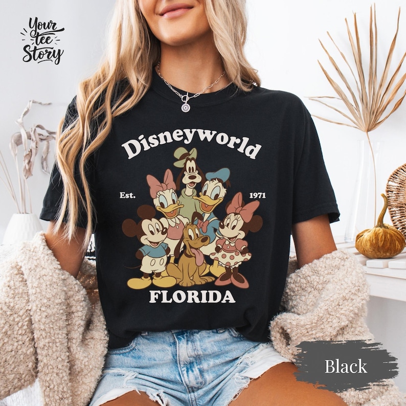 May include: Black t-shirt featuring a vintage-style Disney World graphic with Mickey Mouse, Minnie Mouse, Donald Duck, Daisy Duck, Goofy, and Pluto. The text "Disneyworld Florida Est. 1971" is printed above the characters.