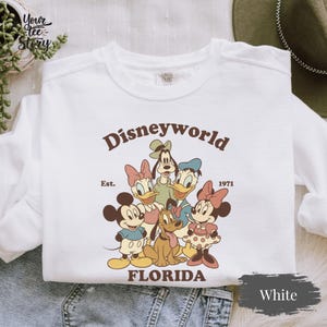 May include: A white ceramic mug with a black handle and the text "But First, Coffee" in a bold, black font. The mug is set against a blurred background, suggesting a cozy setting.