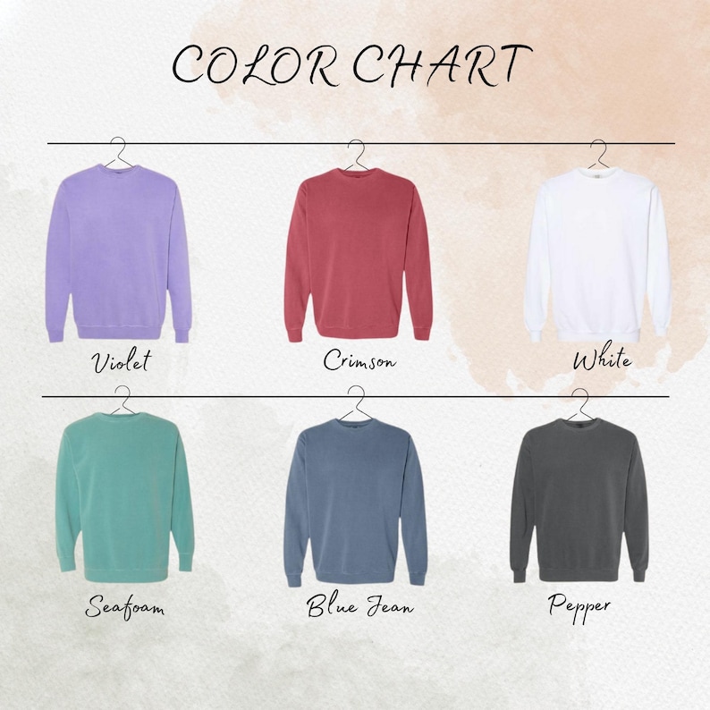 May include: Color chart featuring six crewneck sweatshirts in various colors: violet, crimson, white, seafoam, blue jean, and pepper. Each sweatshirt hangs from a hanger, with the color name displayed below.