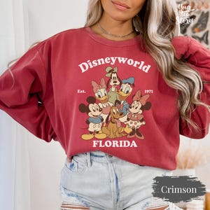 May include: Crimson-colored sweatshirt featuring the text "Disneyworld Florida" with a graphic of Disney characters. The sweatshirt includes the text "Est. 1971".