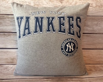 May include: Gray square pillow with the text "NEW YORK YANKEES" in navy blue and white. The pillow also features the New York Yankees logo and the text "AMERICAN LEAGUE EAST DIVISION".