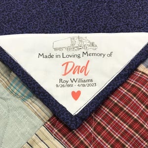 May include: A white triangular quilt label with black text that reads "Made in Loving Memory of Dad Roy Williams 9/26/1951 - 4/19/2023". A red heart is below the text. A black and white drawing of a semi-truck is above the text.