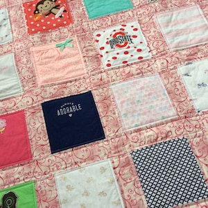 May include: A pink and white baby quilt with a variety of fabric squares, including a square with the text "Always Adorable" in white on a navy blue background.
