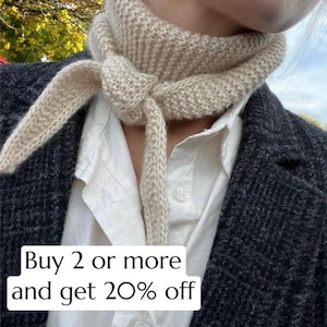 May include: A beige knitted scarf tied in a knot, with long ends hanging down. The scarf is worn over a white collared shirt and a dark gray blazer. The text "Buy 2 or more and get 20% off" is displayed on the image.