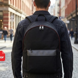 May include: A black backpack featuring a large main compartment with dual silver zips and a smaller front pocket with a grey horizontal accent strip. The bag has padded shoulder straps and a top handle, constructed from a durable fabric material.