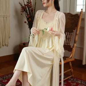 May include: A light yellow nightgown and matching sheer robe with lace trim. The nightgown has a V-neckline and a flowing skirt. The robe has long, flowing sleeves. The outfit is worn with a delicate necklace and a flower.