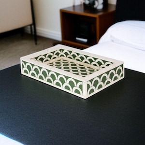 May include: Rectangular decorative tray with a cream-colored frame and a green and cream scallop pattern. The tray is made of a solid material and sits on a black surface. The tray is empty and ready to be used.