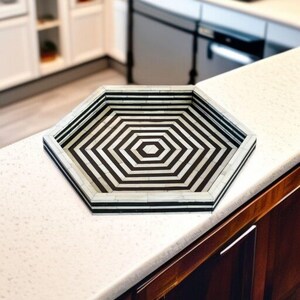 May include: Hexagonal decorative tray with a black and white geometric pattern. The tray has a black border and a repeating pattern of black and white stripes. The tray is made of a durable material and is suitable for serving or display.