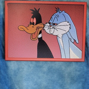 Könnte beinhalten: Gestickter Aufnäher mit Daffy Duck und Bugs Bunny mit roten Augen, vor einem roten Farbverlauf. Der Aufnäher ist rot umrandet und auf einer Jeansjacke befestigt. Die Zeichentrickfiguren sind eng beieinander.