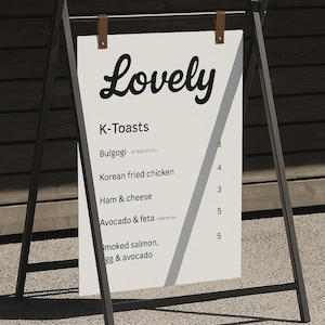 May include: A-frame menu board with the word "Lovely" in cursive script. The menu lists "K-Toasts" with options like Bulgogi, Korean fried chicken, Ham & cheese, Avocado & feta, and Smoked salmon, egg & avocado.