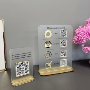 Op de afbeelding: Twee rechthoekige borden van mat acryl met gouden voetstukken. Het linkerbord bevat een QR-code en Russische tekst. Het rechterbord toont vier rijen met gouden iconen, de tekst MAX, Telegram, Sait, Proekt en vier verschillende QR-codes.