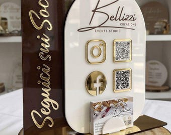 May include: A dual-panel acrylic social media sign featuring a dark brown arched panel with gold text reading Seguici sui Social and a white arched panel with the Bellizzi Creations logo, gold social media icons, QR codes, and a business card holder.