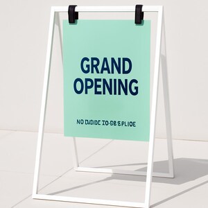 May include: A white A-frame sign with a mint green sign face. The sign reads "GRAND OPENING" in navy blue, with the text "NO DIVIDE TO BE SPLIOE" below. Black clips hold the sign in place.