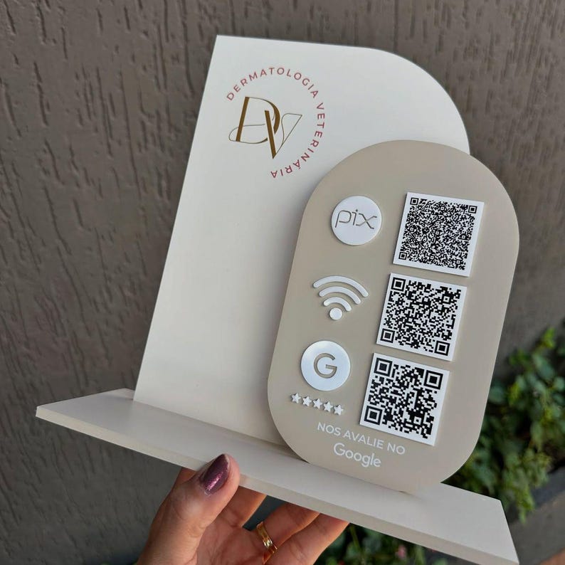 Op de afbeelding: Een beige en wit acrylbord met het logo van Dermatologia Veterin&aacute;ria, drie QR-codes, een Pix-pictogram, een wifi-symbool, een Google-pictogram en vijf sterren met de tekst "NOS AVALIE NO Google" gedrukt op het onderste gedeelte.