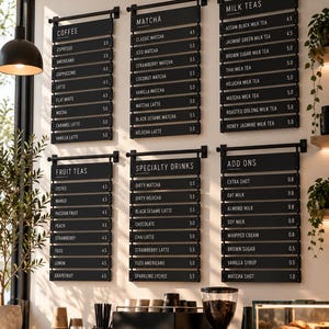 Op de afbeelding: Een wandgemonteerd menubord voor een café met zes zwarte panelen met witte tekst die koffie, matcha, melkthee, vruchtenthee, speciale drankjes en extra's opsommen. Het menu toont verschillende dranknamen en prijzen in een overzichtelijke indeling.