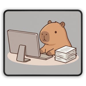 Op de afbeelding: Een rechthoekige muismat met een cartoon capibara die op een computer werkt. De capibara is bruin met een lichtbruin gezicht en zit aan een bureau met een monitor en een stapel papier. De mat heeft een grijze achtergrond en een zwarte rand.
