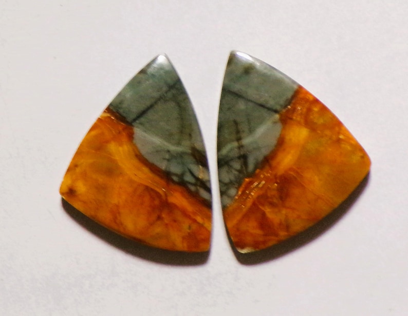 May include: Two triangular cabochons featuring a polished surface with a distinct color split. The top section is a muted grey with dark veining, while the bottom section displays a vibrant, marbled orange and amber pattern with smooth edges.