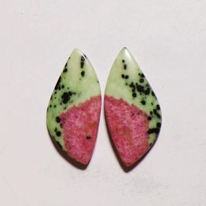 May include: Two polished, teardrop-shaped gemstones featuring a distinct colour pattern. Each stone displays a vibrant pink centre transitioning into a pale mint green outer edge, accented by scattered, irregular black spots across the surface.