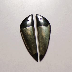 May include: Two teardrop-shaped pendants with a smooth, polished finish. Each piece features a dual-tone design with a dark, glossy black upper section and a metallic, reflective gold-toned lower portion. Both pendants have a small drilled hole.