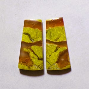 May include: Two trapezoidal cabochons featuring a striking pattern of vibrant lime green mineral inclusions set against a translucent, warm amber-colored background. Each piece has a smooth, polished surface and a small pre-drilled hole at the top.