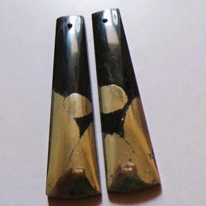May include: A pair of black and gold earrings, each with a trapezoid shape. They feature a hole for hanging. The gold sections have a cracked, distressed look, giving the jewellery a unique texture.
