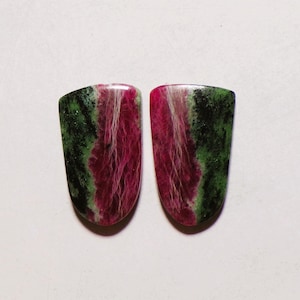 Könnte beinhalten: Zwei schildförmige, polierte Edelsteine mit einer lebendigen Farbkombination aus tiefem Magenta, Waldgrün und Schwarz. Die Steine weisen eine ausgeprägte faserige Textur in den magentafarbenen Bereichen auf, was ein natürliches, marmoriertes Aussehen erzeugt.