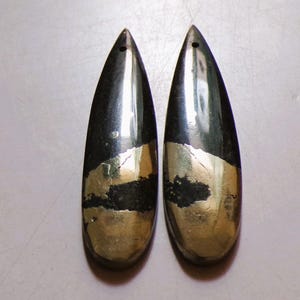 May include: Two teardrop-shaped earrings. Each earring is a mix of black and gold, with a hole at the top for hanging. The gold section is at the bottom, and the black section is at the top. The earrings are smooth and shiny.