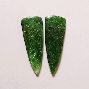 May include: Two polished, green gemstone cabochons with a triangular shape. The gemstones have a sparkling, speckled appearance, with a lighter, translucent area at the pointed end. The background is a plain white.