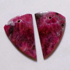 May include: Two polished, semi-circular gemstones in shades of deep pink and burgundy, with a marbled appearance. Each stone has a small hole drilled near the top. These stones are suitable for jewellery making, such as earrings or pendants.
