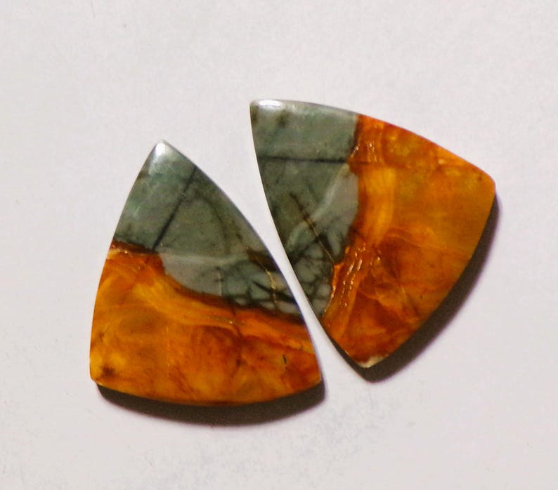 May include: Two triangular cabochons featuring a distinct color split. Each piece displays a smooth, polished surface with a combination of muted grey-green tones and vibrant, swirling orange patterns throughout the stone material.