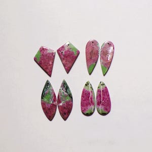 Puede incluir: Ocho colgantes de piedra preciosa rubí zoisita pulidos dispuestos en cuatro pares. Las piedras presentan una mezcla de inclusiones de rubí rosa magenta vibrante y zoisita verde moteada, cada una con un pequeño orificio perforado.