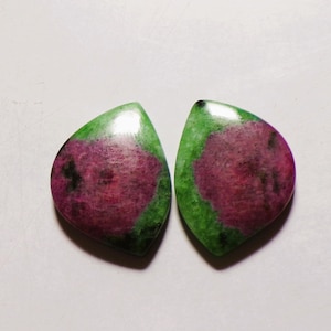 Peut inclure: Deux pierres précieuses en rubis zoïsite polies en forme de goutte, présentant un mélange vibrant de centres magenta-rose profond entourés d'inclusions minérales vert forêt et noires, avec une surface lisse et réfléchissante.
