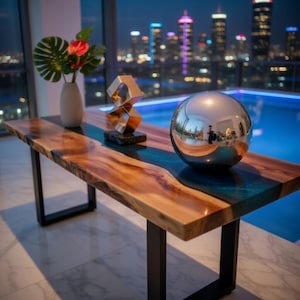 May include: A modern wooden table with a live edge design, featuring a blue resin river. The table has black metal legs and is adorned with a silver sphere, a gold sculpture, and a vase with flowers. The background shows a city skyline at night.