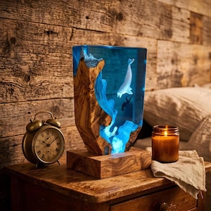 May include: A distinctive lamp with a wooden base and a clear resin body with a blue interior. The resin contains a white whale and a diver. A vintage brass alarm clock and a lit candle are nearby.