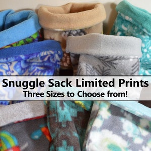 May include: A collection of fleece Snuggle Sacks in various colors and patterns. The sacks have rolled-down cuffs and are made with limited edition prints. The image includes the text "Snuggle Sack Limited Prints Three Sizes to Choose from!"