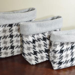May include: A set of three soft fabric storage baskets in varying sizes, featuring a black, white, and gray houndstooth pattern on the exterior and a solid light gray interior lining that folds over the top edge to create a wide cuff.