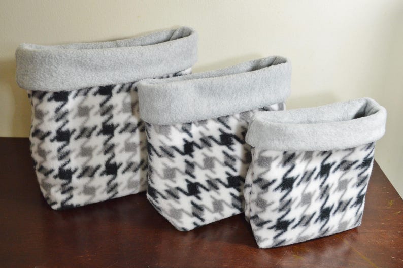 May include: A set of three soft fabric storage baskets in varying sizes, featuring a black, white, and gray houndstooth pattern on the exterior and a solid light gray interior lining that folds over the top edge to create a wide cuff.