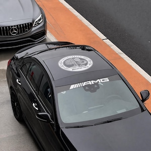 May include: A white ceramic mug with a black handle and the text "But First, Coffee" in a bold, black font. The mug is set against a blurred background, suggesting a cozy setting.