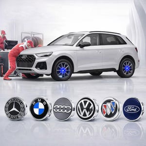 Puede incluir: Un SUV blanco con luces azules en las ruedas. Debajo, seis tapacubos plateados con logotipos de marcas de automóviles: Mercedes-Benz, BMW, Audi, Volkswagen, Buick y Ford. Un mecánico con un mono rojo trabaja en el coche.