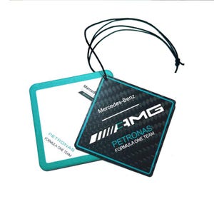 May include: Two square air fresheners with black string. One is white with a teal border and the text "PETRONAS FORMULA ONE TEAM". The other is black with a teal border and the text "Mercedes-Benz AMG PETRONAS FORMULA ONE TEAM".
